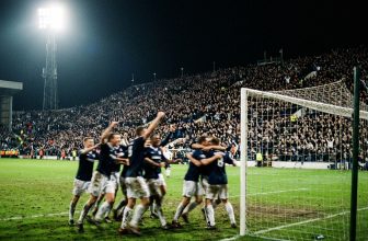 Packed stadium at night as a team celebrates in front of the crowd