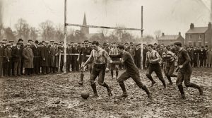 Sepia photograph of a Victorian football match with players in period kit and a laced leather ball